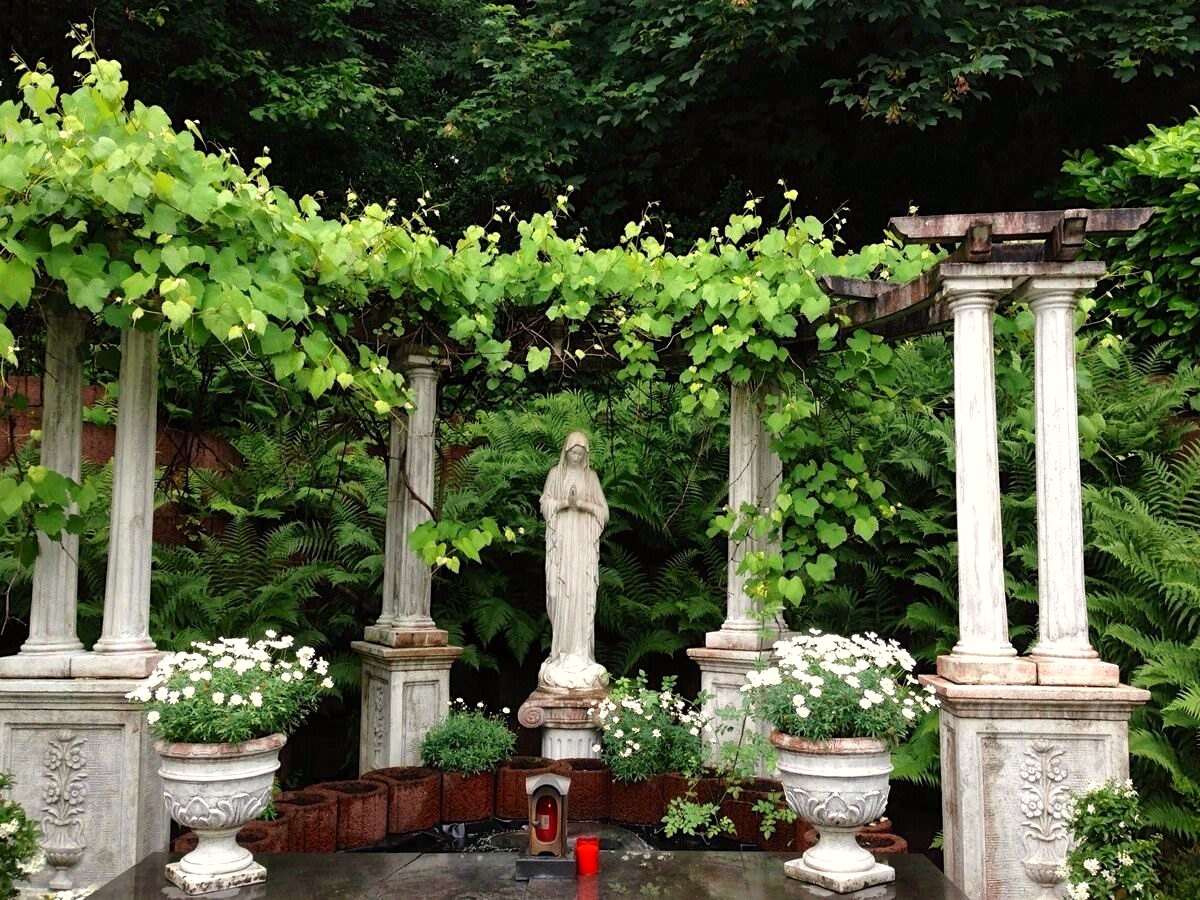 Begrünte Pergola mit Säulen, Figur und bepflanzten Kübeln im Garten