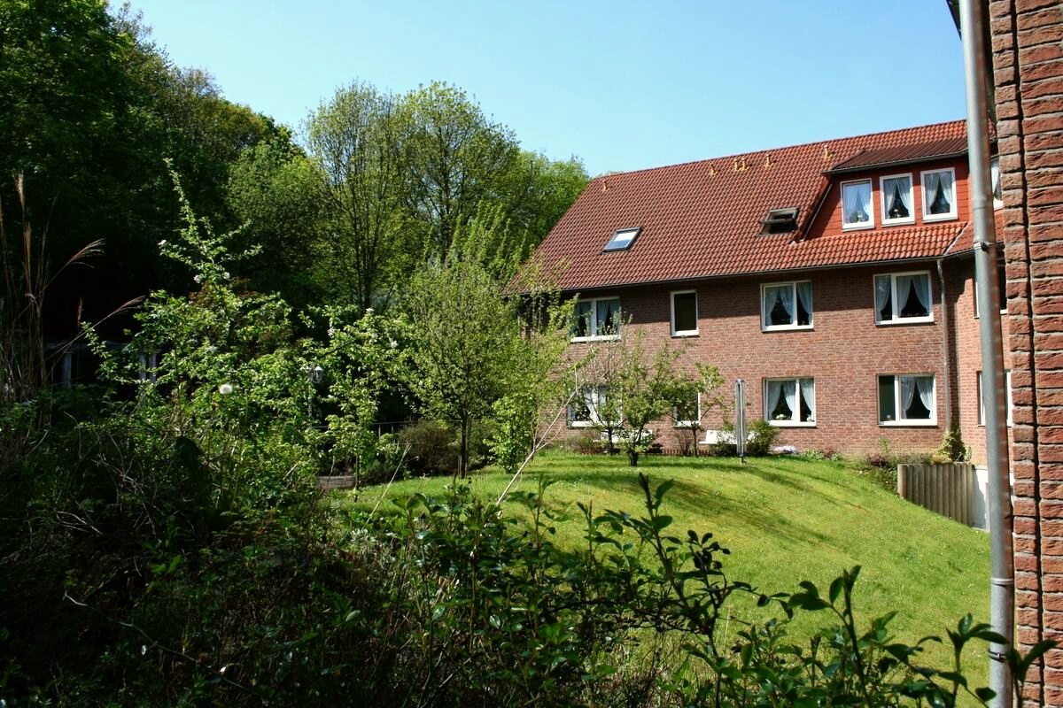 Blick auf das Gebäude aus dem umgebenden Grün mit Wiese und Bäumen